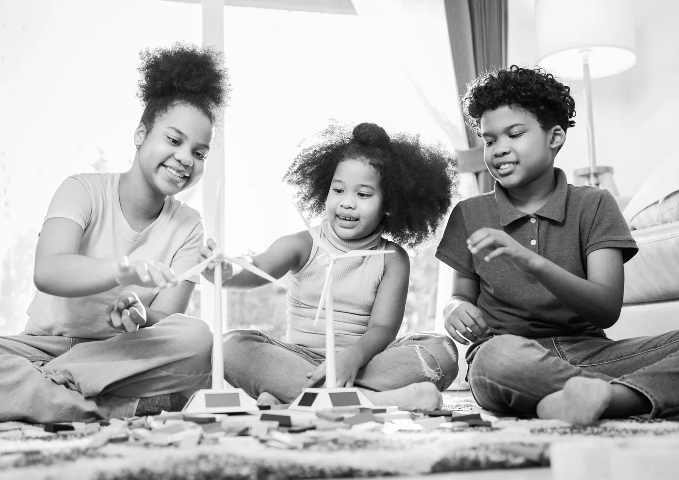 Three children sitting on the floor playing with building blocks and toy wind turbines